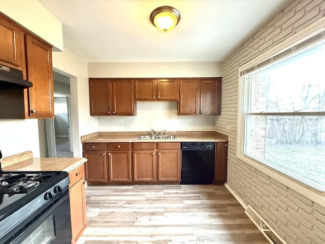 kitchen with black appliances, plenty of natural light, brick wall, and light hardwood / wood-style flooring