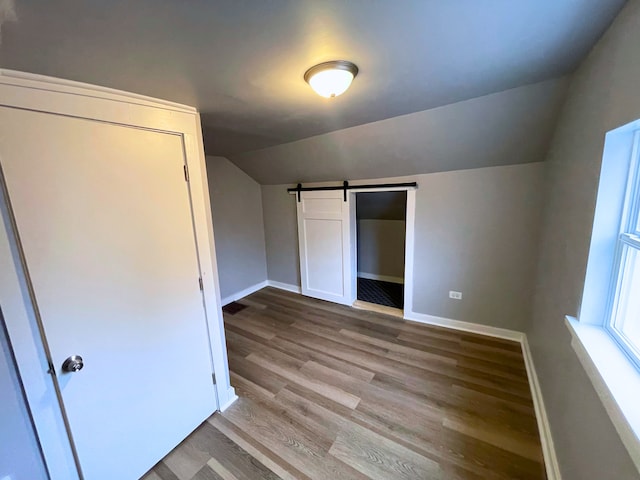 additional living space featuring a barn door, light hardwood / wood-style floors, and lofted ceiling