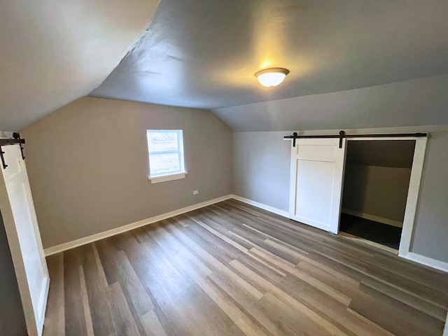 bonus room with a barn door, hardwood / wood-style floors, and vaulted ceiling