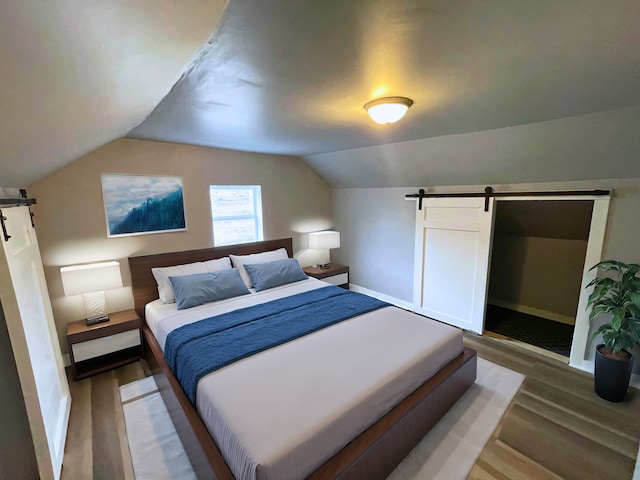 bedroom with wood-type flooring, a barn door, and lofted ceiling