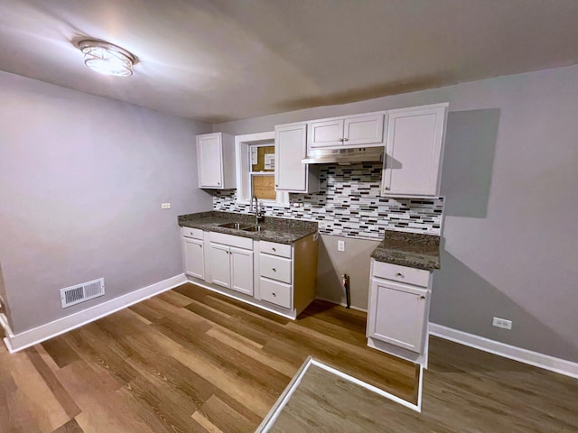 kitchen with sink, tasteful backsplash, dark stone counters, wood-type flooring, and white cabinets