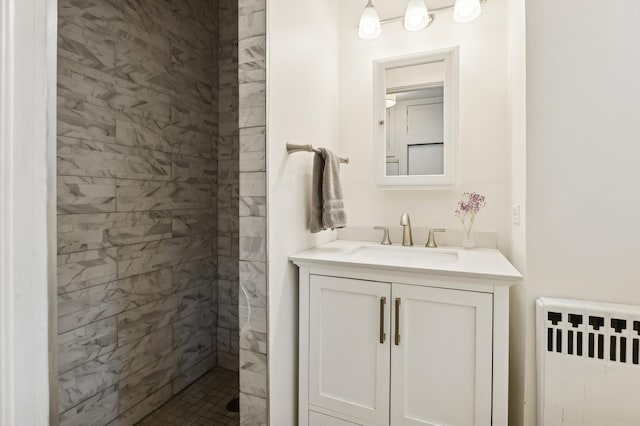 bathroom with a tile shower, vanity, and radiator