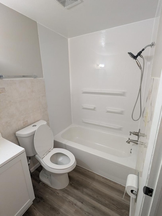 full bathroom featuring washtub / shower combination, hardwood / wood-style floors, toilet, vanity, and tile walls