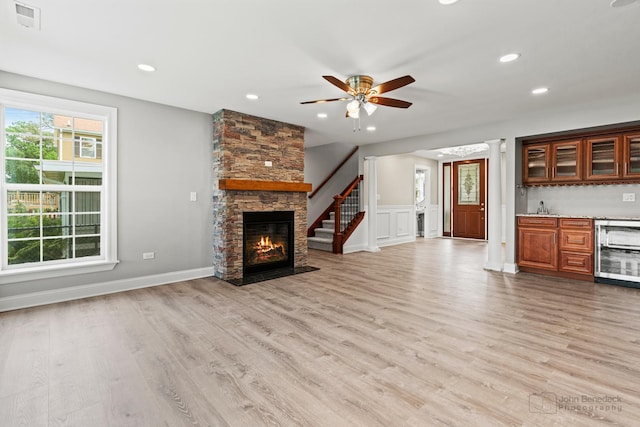 unfurnished living room featuring wet bar, beverage cooler, a fireplace, and light hardwood / wood-style flooring