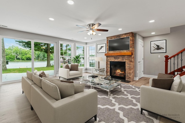 living room with ceiling fan, a stone fireplace, and light wood-type flooring