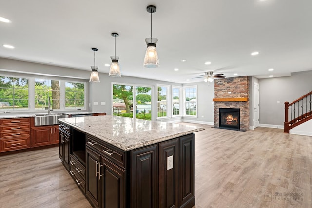 kitchen featuring dark brown cabinetry, sink, hanging light fixtures, light hardwood / wood-style flooring, and light stone countertops