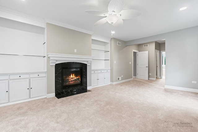 unfurnished living room with built in shelves, a fireplace, light colored carpet, and ceiling fan