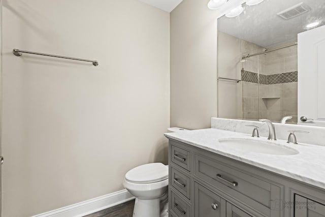 bathroom with hardwood / wood-style flooring, vanity, a tile shower, and toilet