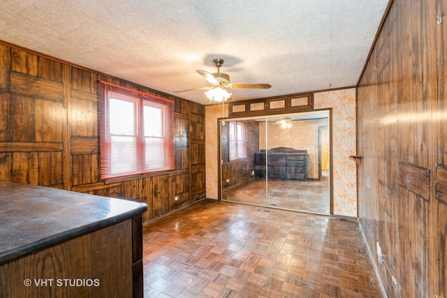 interior space with wood walls, ceiling fan, a textured ceiling, and parquet flooring