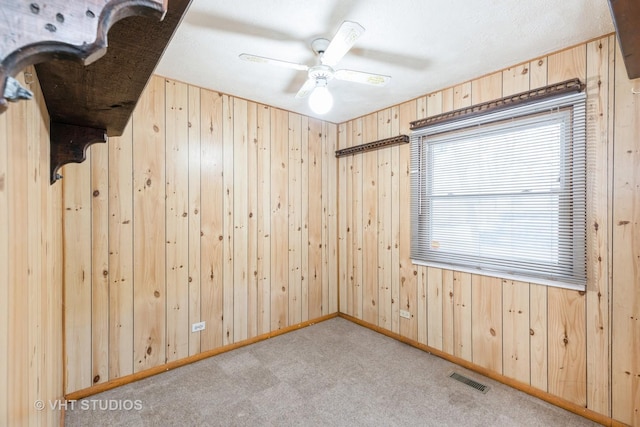 spare room featuring ceiling fan, wooden walls, and light carpet