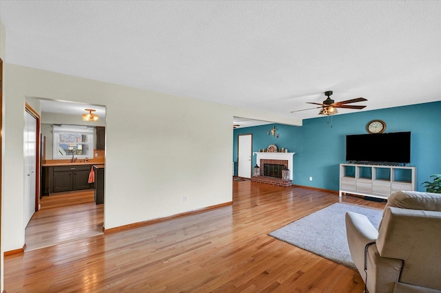 living room with ceiling fan, light hardwood / wood-style floors, sink, and a fireplace