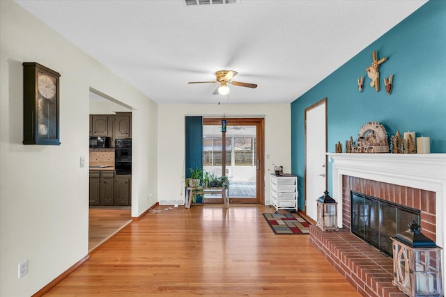 living room featuring ceiling fan, light wood-type flooring, a textured ceiling, and a brick fireplace