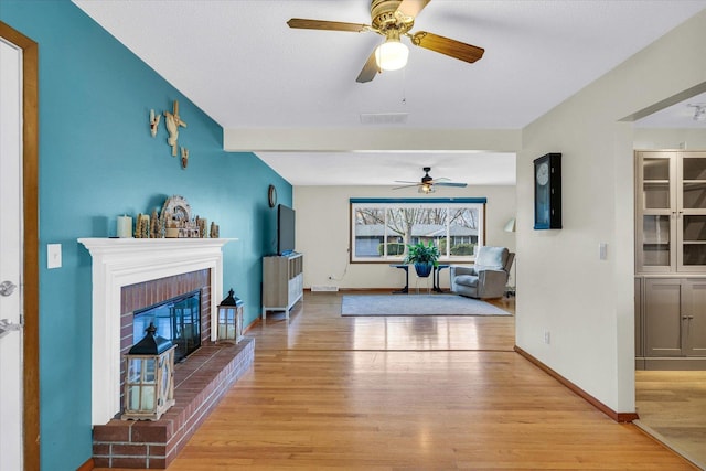 living room featuring a fireplace, light wood-type flooring, ceiling fan, and beamed ceiling