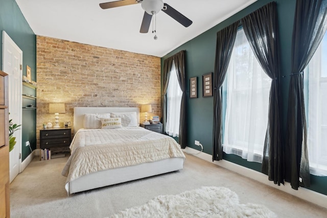 carpeted bedroom featuring multiple windows, ceiling fan, and brick wall