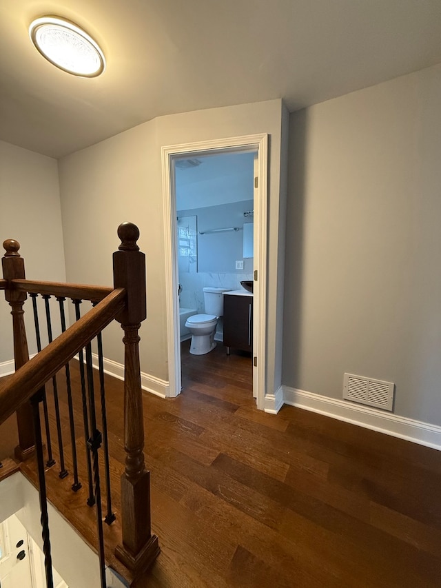 hall with dark wood-style flooring, an upstairs landing, visible vents, and baseboards