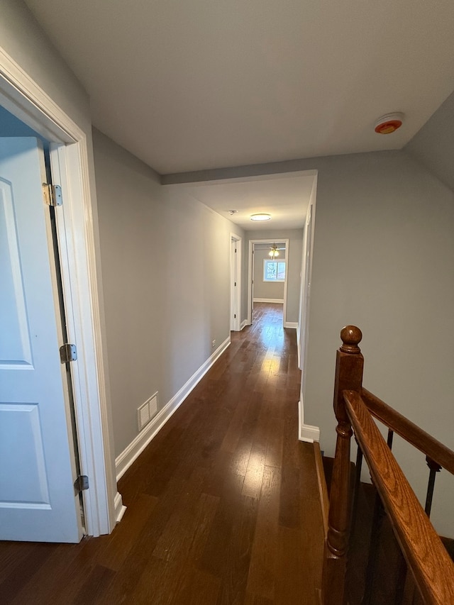 hall featuring dark wood-style floors, baseboards, visible vents, and an upstairs landing