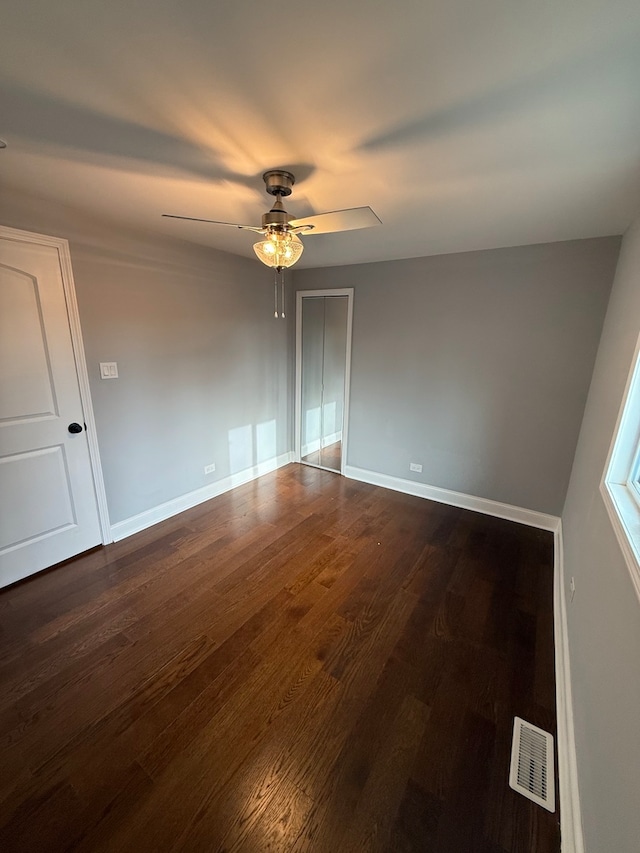 spare room featuring dark wood-type flooring, visible vents, baseboards, and a ceiling fan