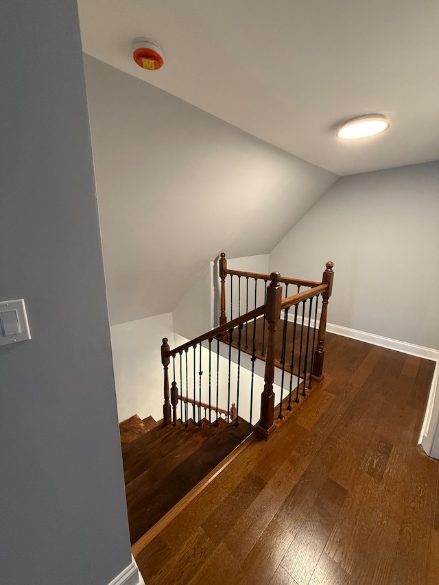 stairway featuring lofted ceiling, baseboards, and wood finished floors