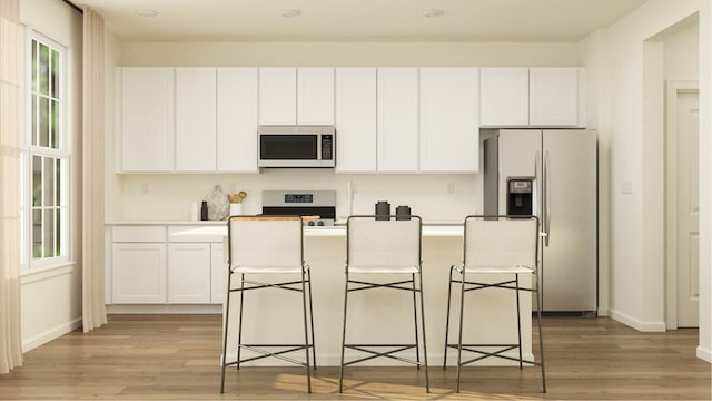 kitchen with light wood-type flooring, white cabinetry, an island with sink, and appliances with stainless steel finishes