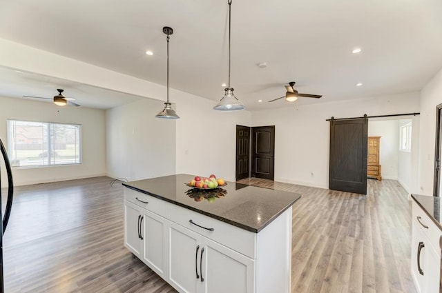 kitchen featuring ceiling fan, a barn door, light wood-type flooring, decorative light fixtures, and white cabinetry