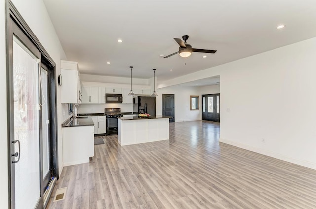 kitchen with light wood-type flooring, sink, black appliances, decorative light fixtures, and white cabinets