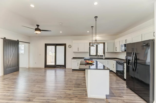 kitchen with black appliances, a barn door, decorative light fixtures, light hardwood / wood-style floors, and white cabinetry