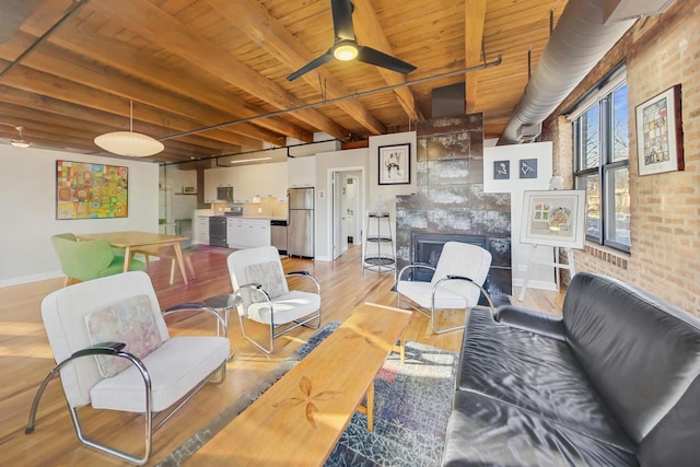 living room with wood ceiling, light hardwood / wood-style flooring, a tile fireplace, ceiling fan, and beam ceiling