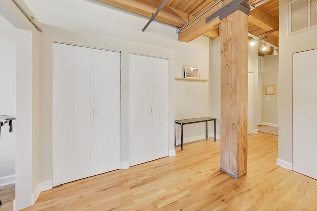 interior space featuring two closets, hardwood / wood-style floors, wooden ceiling, and beam ceiling