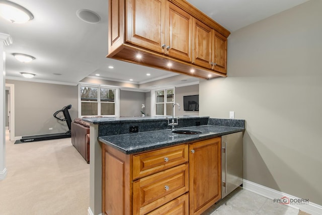 kitchen featuring sink, light carpet, ornamental molding, kitchen peninsula, and dark stone counters