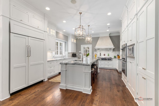 kitchen with a kitchen breakfast bar, custom range hood, white cabinets, a center island with sink, and decorative backsplash