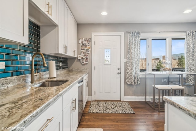 kitchen featuring backsplash, sink, light stone countertops, white cabinets, and dark hardwood / wood-style flooring