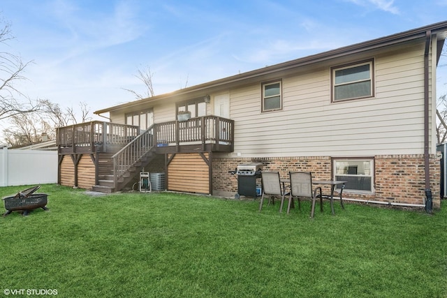 back of property featuring a deck, a lawn, and a fire pit