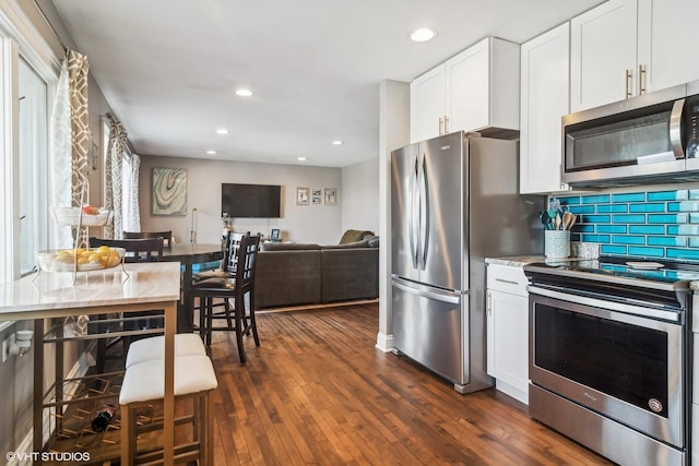 kitchen with dark hardwood / wood-style floors, stainless steel appliances, white cabinetry, and tasteful backsplash