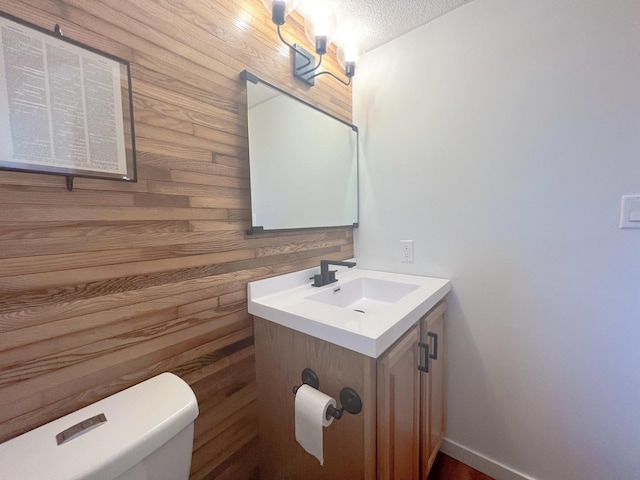 bathroom with vanity, toilet, a textured ceiling, and wooden walls