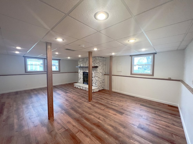 basement with a drop ceiling, dark hardwood / wood-style floors, a stone fireplace, and a wealth of natural light