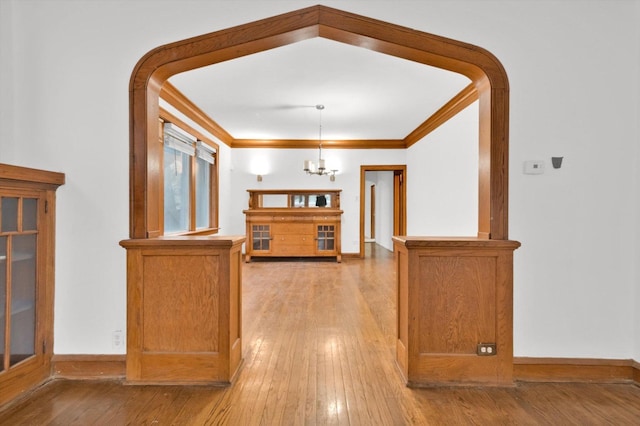 corridor with ornamental molding, a notable chandelier, and light wood-type flooring