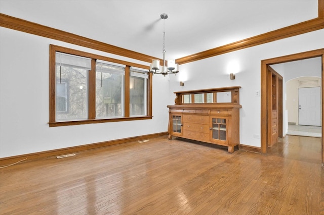 unfurnished living room featuring a chandelier, wood-type flooring, and ornamental molding