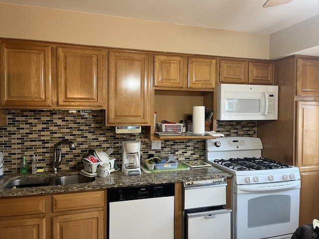 kitchen featuring backsplash, sink, dark stone counters, and white appliances