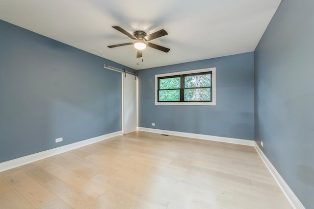 unfurnished room featuring a barn door, ceiling fan, and light hardwood / wood-style flooring