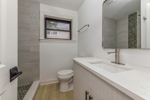 bathroom with tiled shower, toilet, vanity, and hardwood / wood-style flooring