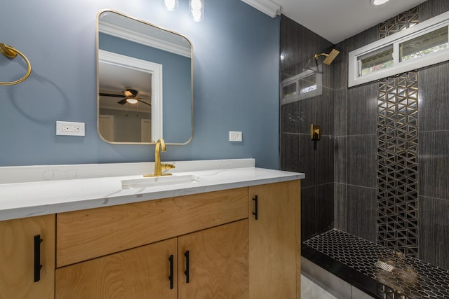 bathroom with ceiling fan, vanity, ornamental molding, and tiled shower