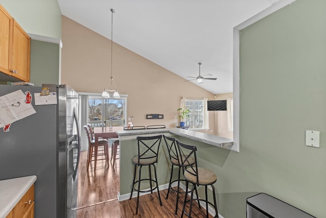 kitchen with kitchen peninsula, a breakfast bar, ceiling fan with notable chandelier, vaulted ceiling, and stainless steel refrigerator