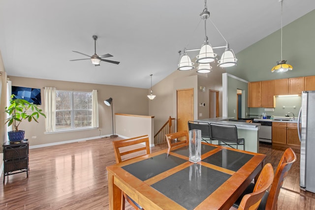 dining space featuring wood-type flooring, ceiling fan with notable chandelier, high vaulted ceiling, and sink