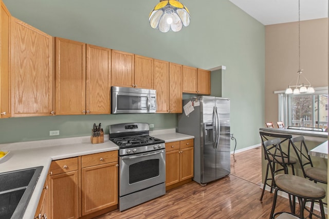 kitchen with sink, hanging light fixtures, stainless steel appliances, a towering ceiling, and wood-type flooring