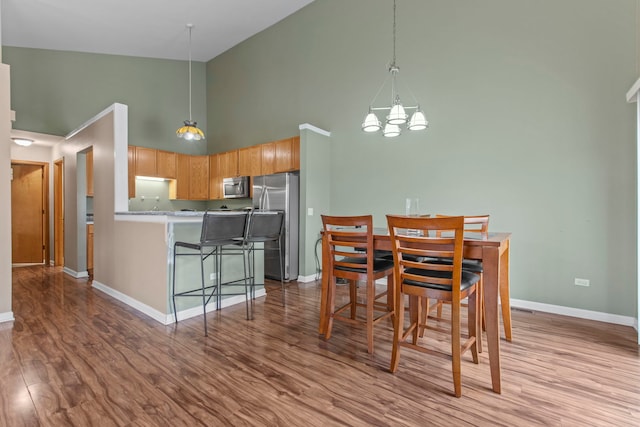 dining space with light wood-type flooring, an inviting chandelier, and high vaulted ceiling