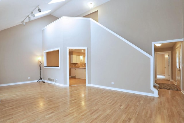 unfurnished living room with light hardwood / wood-style floors, a skylight, high vaulted ceiling, and track lighting