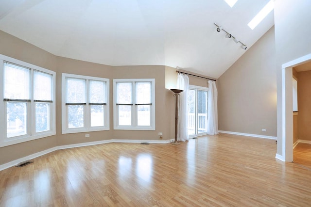 unfurnished living room featuring light wood-type flooring, rail lighting, high vaulted ceiling, and a skylight