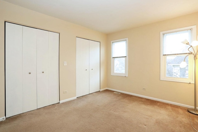 unfurnished bedroom with light carpet and multiple closets