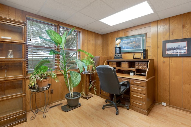 home office featuring a paneled ceiling, light hardwood / wood-style flooring, and wooden walls