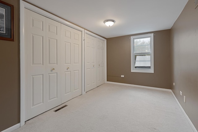 unfurnished bedroom with two closets and light colored carpet